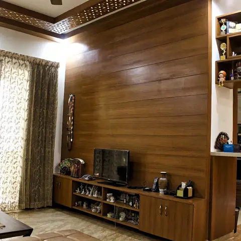 Living room with a full wood-plank panelled TV wall, a wood console displaying curios, jaali-cut cove ceiling trim