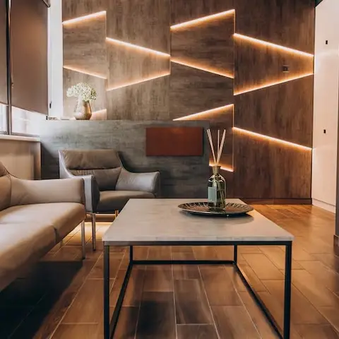 Living room with a geometric backlit textured concrete-finish feature wall behind leather sofas and a marble-top black-frame coffee table on wood plank flooring