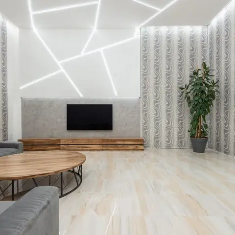 Living room with a geometric linear-light ceiling feature above a floating wood TV console, framed by beige marble flooring and swirl-patterned curtains.