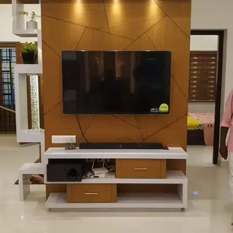 Living room with a geometric wood-panel TV feature wall lit by spotlights, beside a white jaali display partition