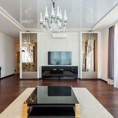 Living room with a glossy backlit stretch ceiling, a tiered crystal chandelier, a black-and-gold coffee table on a cream rug