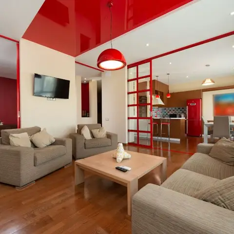 Living room with a glossy red ceiling and accent wall, grey sofas around a wood coffee table, opening to a red-framed glass partition toward the kitchen.