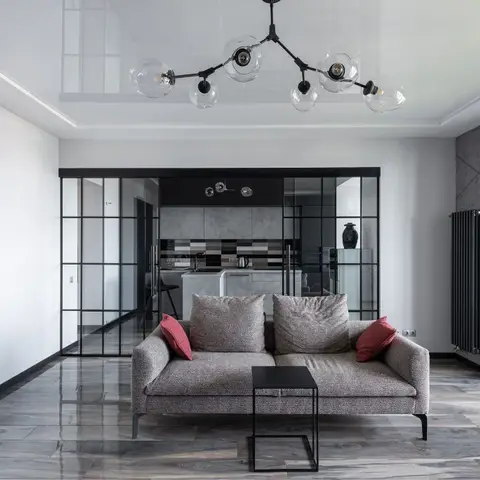 Living room with a glossy stretch ceiling, a branching molecular pendant light, a grey sofa with red accent cushions