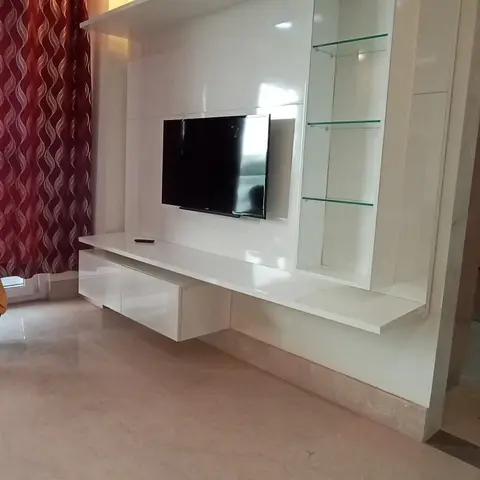 Living room with a glossy white floating TV unit featuring a glass-shelved display tower, paired with maroon patterned curtains.