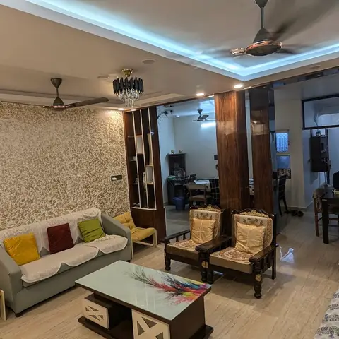 Living room with a gold textured wallpaper accent wall, LED cove-lit ceiling and crystal chandelier, slipcovered grey sofas with mixed cushions