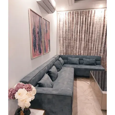 Living room with a grey-blue L-shaped sofa, a two-panel abstract pink-and-charcoal painting on the wall, sheer gold-patterned floor-length curtains