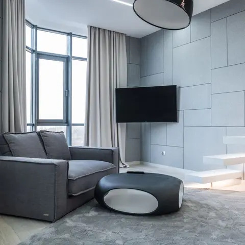 Living room with a grey fabric-panelled feature wall holding a wall-mounted TV, a charcoal sofa, a sculptural black-and-white oval coffee table