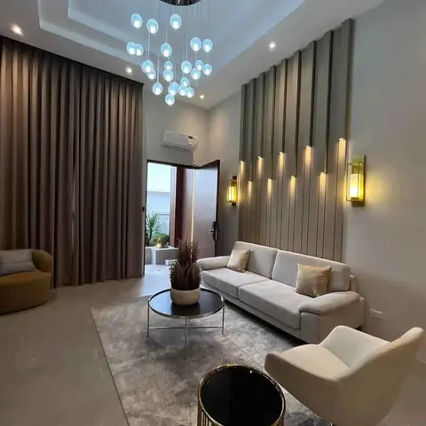 Living room with a grey fabric sofa and cream armchair around a round black coffee table, beneath a cascading bubble chandelier