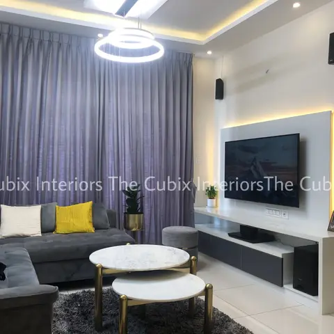 Living room with a grey L-shaped sectional sofa, yellow and white cushions, a backlit white TV feature wall, and round marble-and-gold nesting coffee tables.