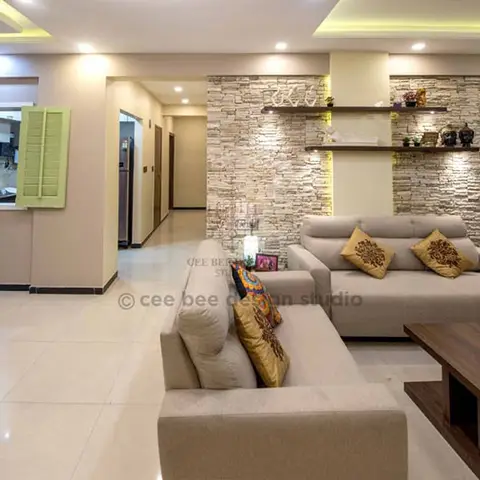 Living room with a grey L-shaped sofa with mustard cushions facing a stone-clad accent wall with floating lit display shelves