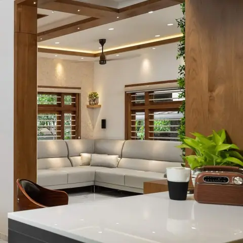 Living room with a grey L-shaped leather sectional under a wood-beam coffered ceiling, seen past a dark kitchen counter with a vintage radio.