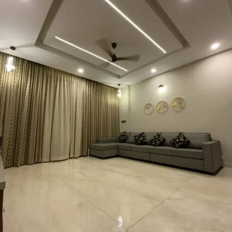 Living room with a grey L-shaped sectional sofa, a trio of round decorative wall plates, gold patterned curtains, and a linear cove-lit false ceiling.