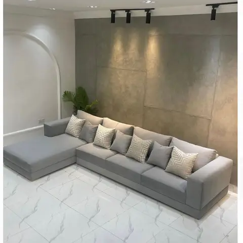 Living room with a grey L-shaped sectional sofa and patterned cushions set against a textured stone-look feature wall with track spotlights.