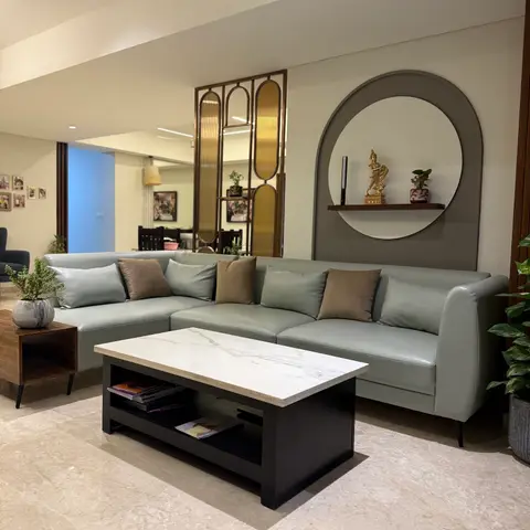 Living room with a grey leather sectional sofa and marble-top coffee table, a brass-framed reeded-glass screen beside a circular wall niche displaying a brass