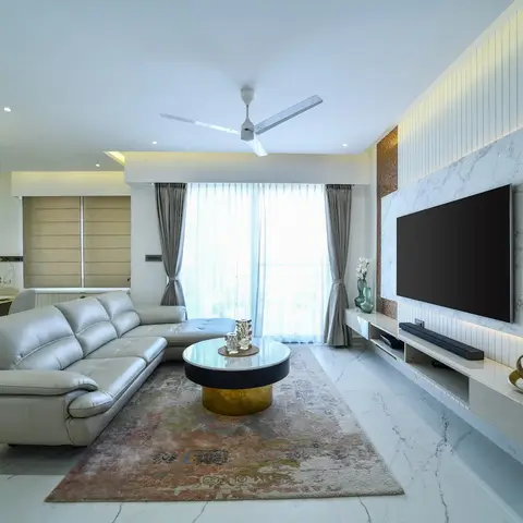 Living room with a grey leather sectional sofa facing a round marble-and-brass coffee table, set before a backlit marble-clad TV wall with a floating console