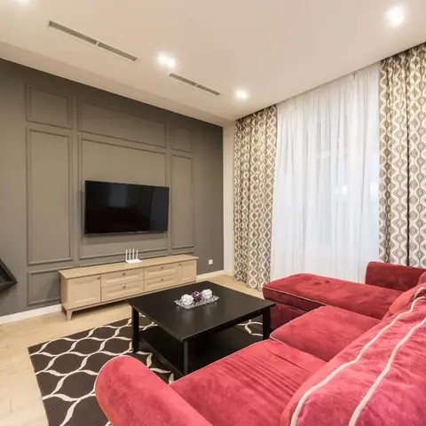 Living room with a grey moulded TV feature wall, a black modern flue element, and a red velvet sectional sofa on a diamond-pattern rug.