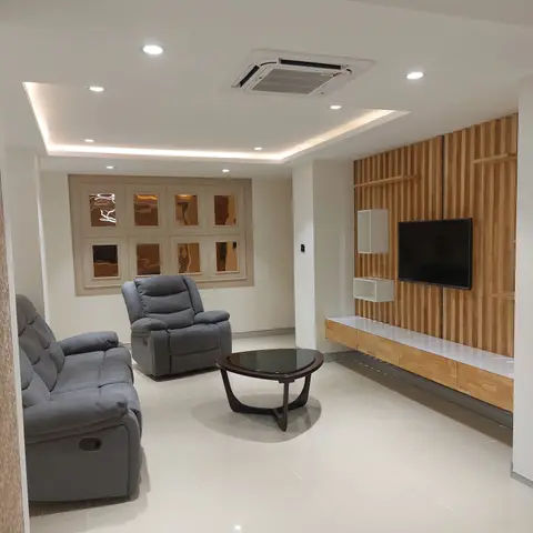 Living room with a grey reclining sofa set and round dark-wood coffee table facing a wood-slat TV feature wall