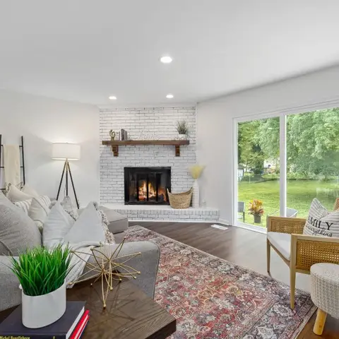 Living room with a grey sectional sofa, a whitewashed brick fireplace, a rattan accent chair, and a sliding glass door opening to the backyard.