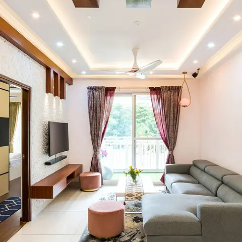 Living room with a grey sectional sofa and blush-pink ottomans facing a floating wood console on a stone-clad wall