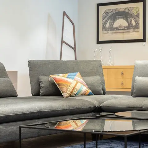 Living room with a grey sectional sofa, black-frame glass coffee tables and a sunburst mirror above a mid-century console.