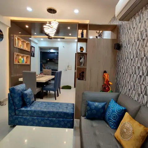 Living room with a grey sofa and blue chaise against a geometric grey-and-gold wallpaper wall, a display shelf with curio niches