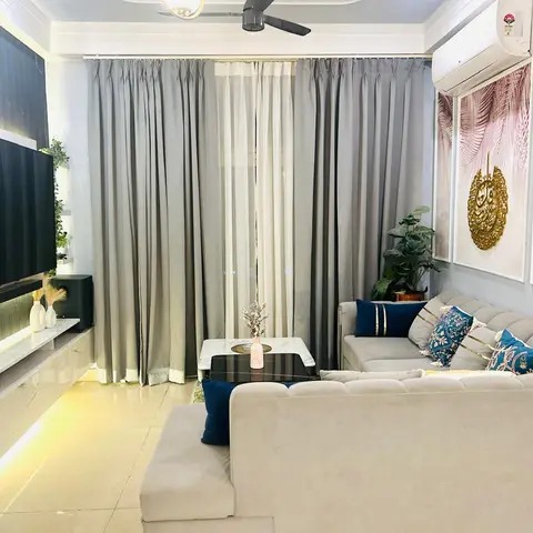 Living room with a grey tufted L-shaped sofa in navy and gold cushions, a fluted-panel TV wall with a backlit floating console