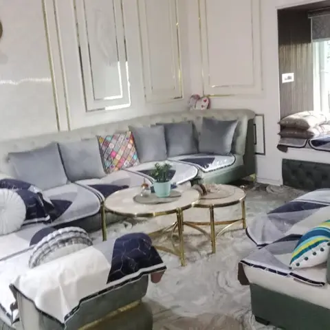 Living room with a grey tufted sectional sofa and matching armchairs draped in throws, gold-outlined wall panel mouldings