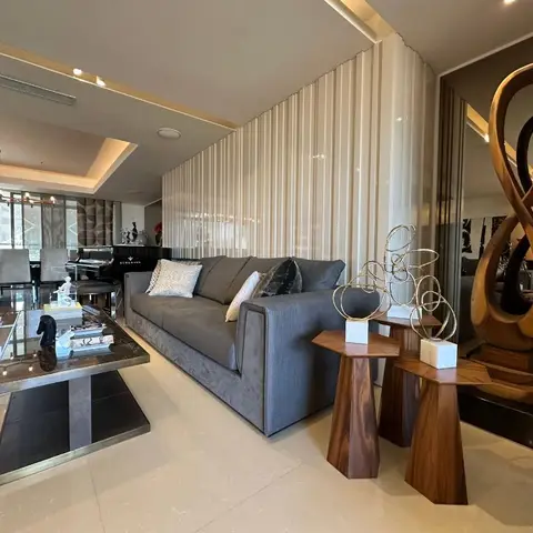 Living room with a grey velvet sofa, black marble coffee table and sculptural wood side-table decor, dining and a piano visible beyond.