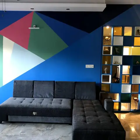 Living room with a hand-painted geometric mural of blue, teal and crimson triangles behind a charcoal tufted L-sofa