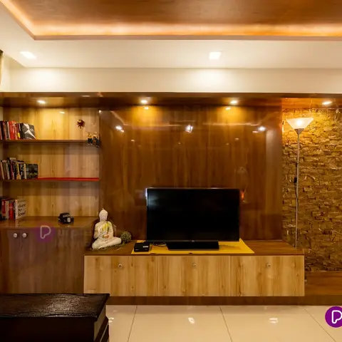 Living room with a high-gloss wood-veneer TV unit wall flanked by an exposed stacked-stone accent pillar, open wood bookshelves with novels