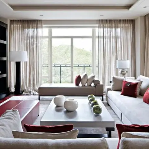 Living room with a large cream sectional sofa dressed in red accent cushions, sheer curtains at full-height French doors