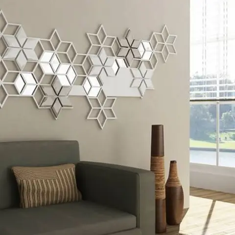 Living room with a large geometric star-shaped mirror wall installation above a charcoal sofa, tall ceramic floor vases beside a garden-view window.