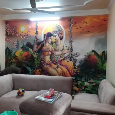 Living room with a large Radha-Krishna devotional mural wallpaper as the feature wall behind a grey sectional sofa.