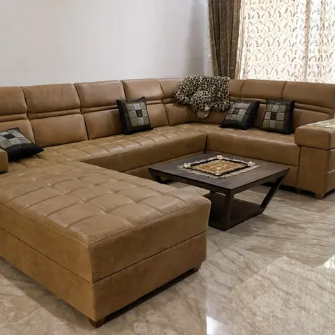 Living room with a large tan leather U-shaped sectional sofa, a dark wood coffee table on a black metal X-frame with a small dhurrie runner