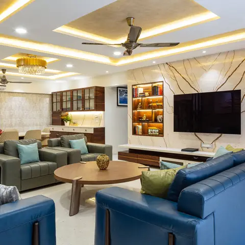 Living room with a layered gold cove-lit false ceiling, a book-and-curio niche wall in marble-clad panelling beside a wall-mounted TV