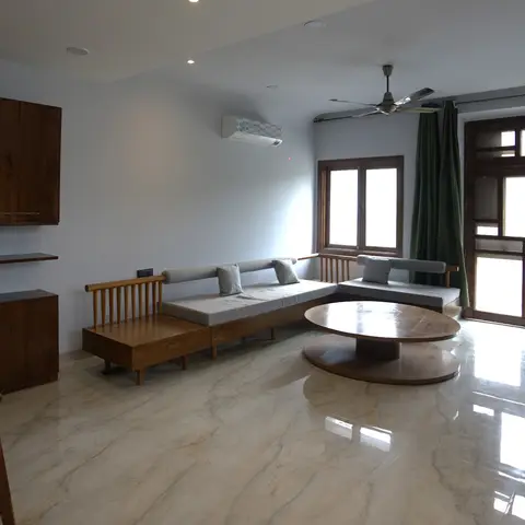 Living room with a low teak spindle-back sofa, round pedestal coffee table and glossy veined marble flooring opening onto a wood-framed balcony door.