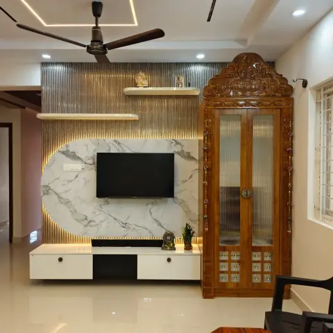 Living room with a marble and fluted-metal TV feature wall beside a hand-carved wooden pooja cabinet with glass doors and brass bells