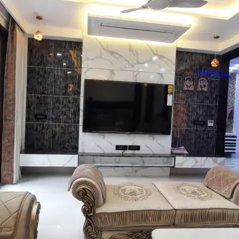 Living room with a marble and dark stone-clad TV feature wall, cove-lit ceiling and an ornate carved wood sofa set with tufted gold-trimmed upholstery