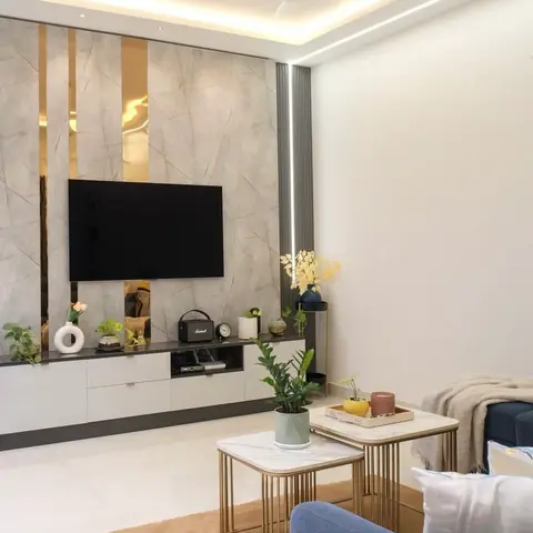 Living room with a marble-slab TV feature wall inlaid with vertical brass strips, a two-tone floating console, and gold-framed nested marble coffee tables
