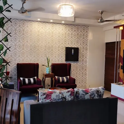 Living room with a maroon-and-gold backlit TV feature wall, damask wallpaper accent wall, and wingback chairs flanking a faux-vine room divider.