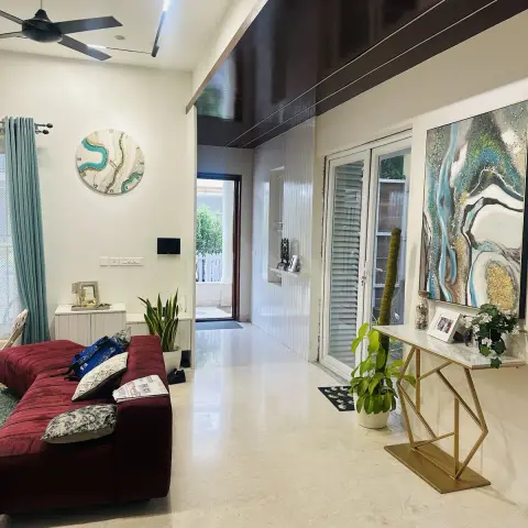 Living room with a maroon velvet sofa, teal curtains, and a round wall clock, opening through a hallway to a gold geometric console table with abstract art