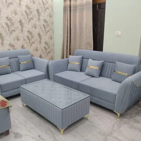 Living room with a matching powder-blue tufted velvet sofa set with gold-trim cushions and a channel-tufted coffee table, against floral wallpaper.