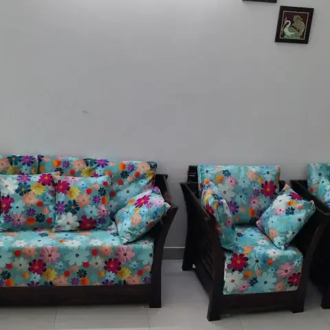 Living room with a matching wood-frame three-piece sofa set upholstered in a bright floral print against a plain white wall
