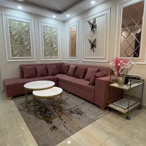 Living room with a mauve L-shaped sofa, nesting marble-top coffee tables, and a wall of moulded picture-frame panels holding botanical prints and a diamond-cut