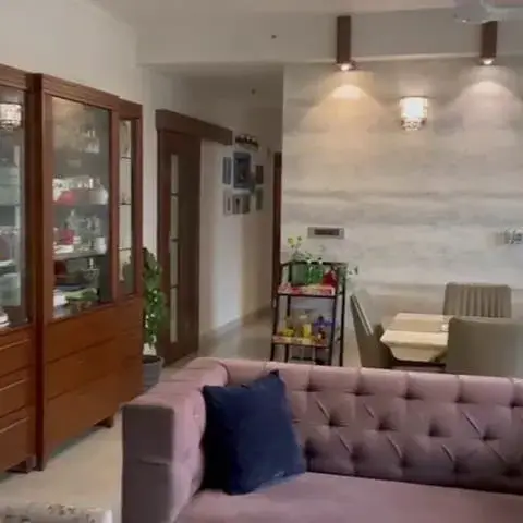 Living room with a mauve tufted sofa and a floral wingback chair beside a wood glass-front crockery cabinet