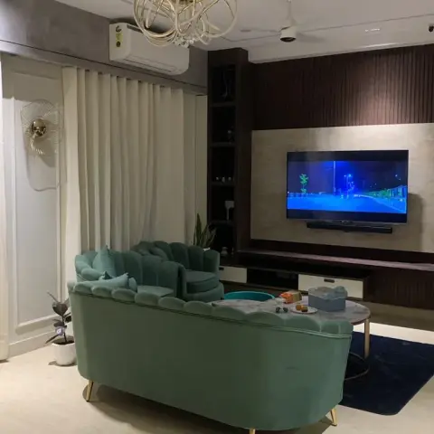 Living room with a mint-green scalloped velvet sofa, a stone-and-wood TV feature wall, a gold branch chandelier, and a round marble coffee table on a navy rug.
