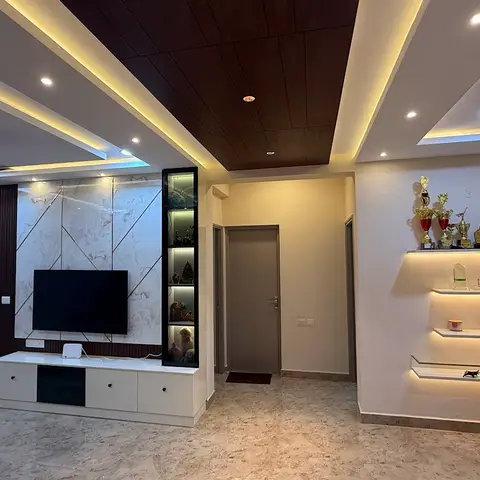 Living room with a multi-level cove-lit false ceiling dropping to a wood-panel soffit over a marble-clad TV unit