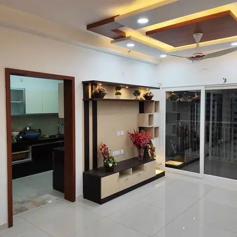 Living room with a multi-tier wood-trimmed POP ceiling, an open-shelf TV display console styled with plants, and sliding doors to a balcony.