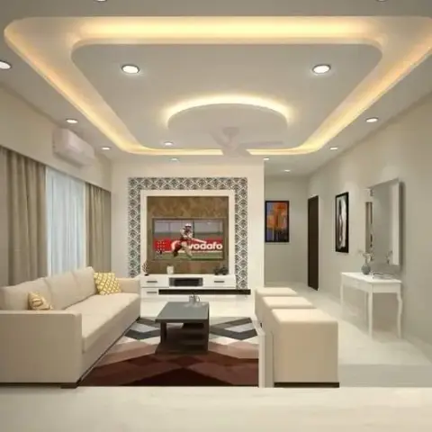 Living room with a multi-tier cove-lit false ceiling over a patterned mosaic TV feature wall, cream sofas and a geometric diamond-pattern rug.