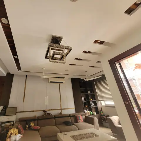Living room with a multi-tier false ceiling and wood inlay accents, a geometric crystal chandelier